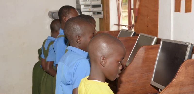 Hadassah students in blue uniforms stand at a row of old desktop computers.